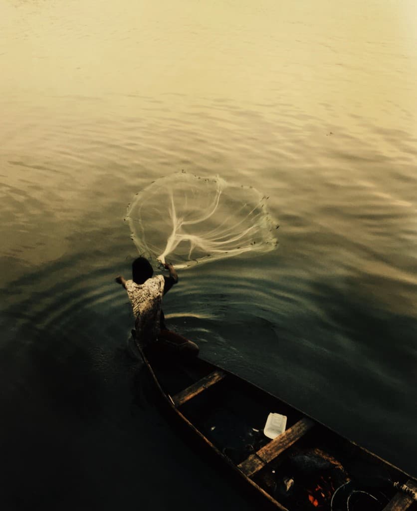 A fisherman casts a net from a canoe at dusk.