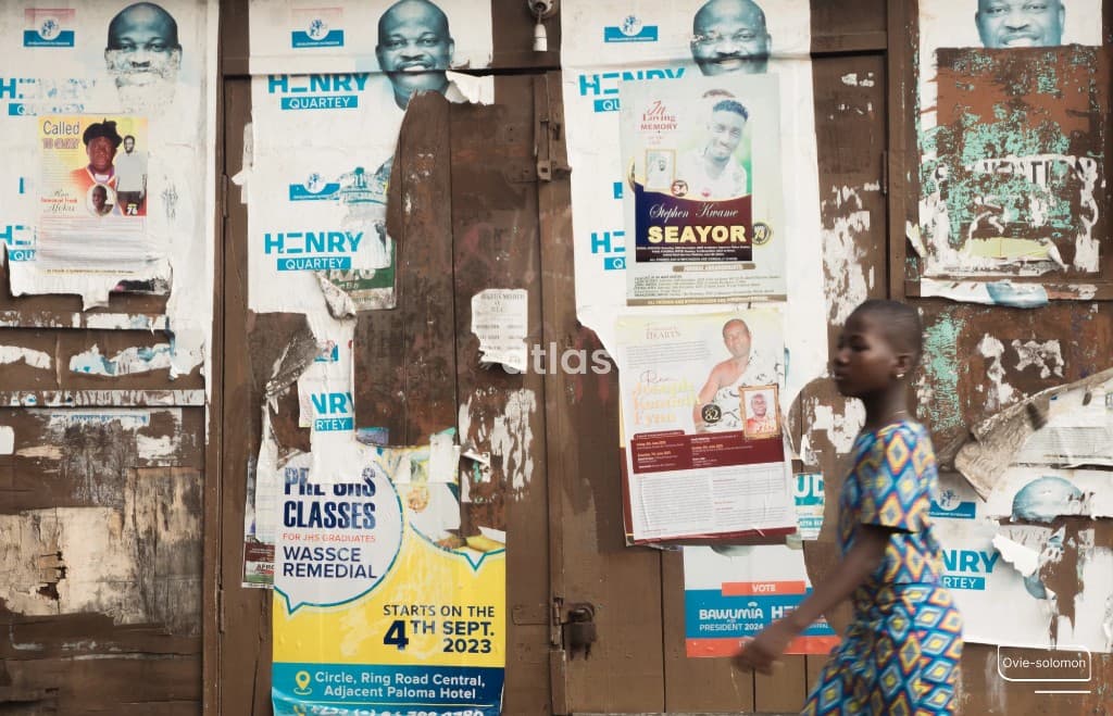 A girl walks past a wall of layered street posters.